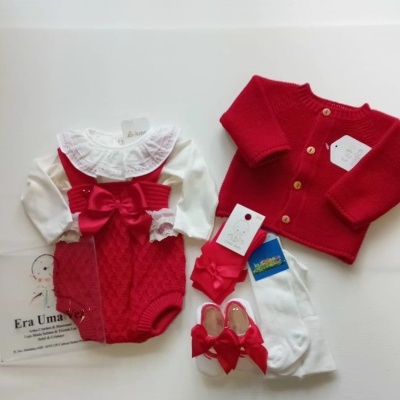 Conjunto de roupa de bebé com jardineira vermelha, body branco com babado, casaco vermelho, meias e sapatinhos em fundo branco