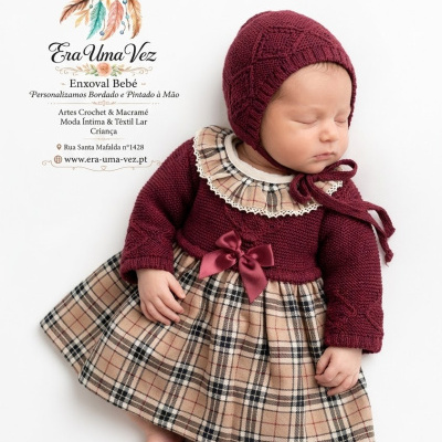 Bebé com vestido xadrez bege e vermelho e gorro tricotado vermelho a dormir em fundo branco