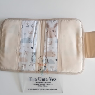 Organizador bege claro com bolsos transparentes e fundo estampado, sobre superfície branca com saco plástico com inscrições.