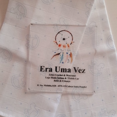 Pano branco com padrão quadriculado e desenhos de cavalinho de baloiço, etiqueta com apanhador de sonhos e texto da marca Era Uma Vez.