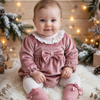 Bebé com vestido rosa e meias com laços sentada em tapete branco com decoração natalícia ao fundo