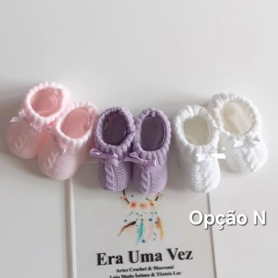 Três pares de sapatinhos de bebé em crochet rosa lilás branco com laços pequenos sobre superfície branca com texto