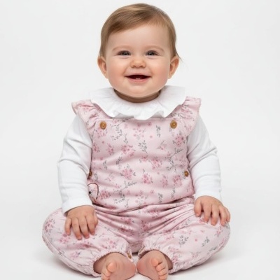 Bebé sentado com macacão rosa floral e camisa branca com gola babada