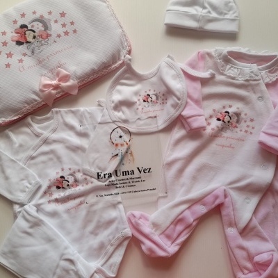 Conjunto de roupa de bebé com macacão, body, babete, manta e gorro branco e rosa com personagem infantil e estrelas.