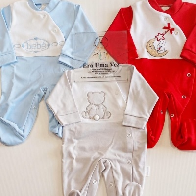 Roupas de bebé em azul claro, vermelho e cinza com bordados e botões de pressão sobre fundo branco