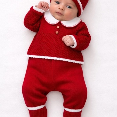 Bebé com roupa vermelha de malha e detalhes em branco, deitado sobre fundo branco.