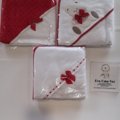Três toalhas de bebé embaladas com detalhes vermelhos e brinquedo bordado, com cartão à direita