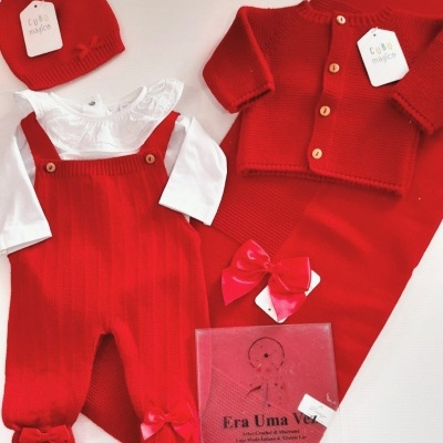 Conjunto de roupa de bebê vermelho com casaco, jardineira, camisa branca, gorro e mantinha.