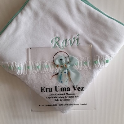 Toalha branca com bordado e placa informativa sobre superfície branca