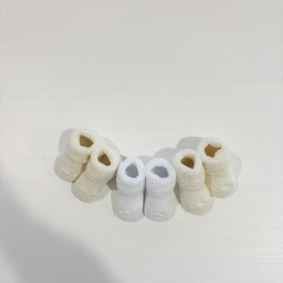 Três pares de meias de bebé felpudas em tons bege e branco sobre fundo branco.
