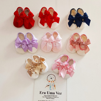 Sapatinhos de bebé brancos com laços coloridos dispostos em fila sobre fundo branco.