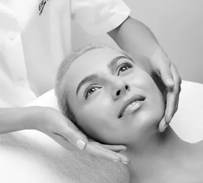 Mulher deitada recebendo tratamento facial com mãos a segurarem-lhe o rosto