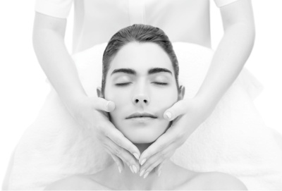 Mulher a receber massagem facial com terapeuta de unhas brancas em fundo branco