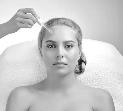 Mulher deitada com conta-gotas perto da testa num fundo neutro