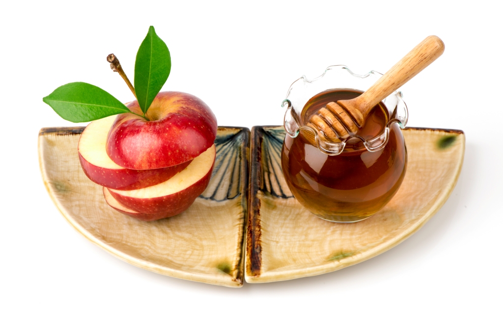 Tábua de cerâmica com maçã cortada e pote de mel com colher de madeira