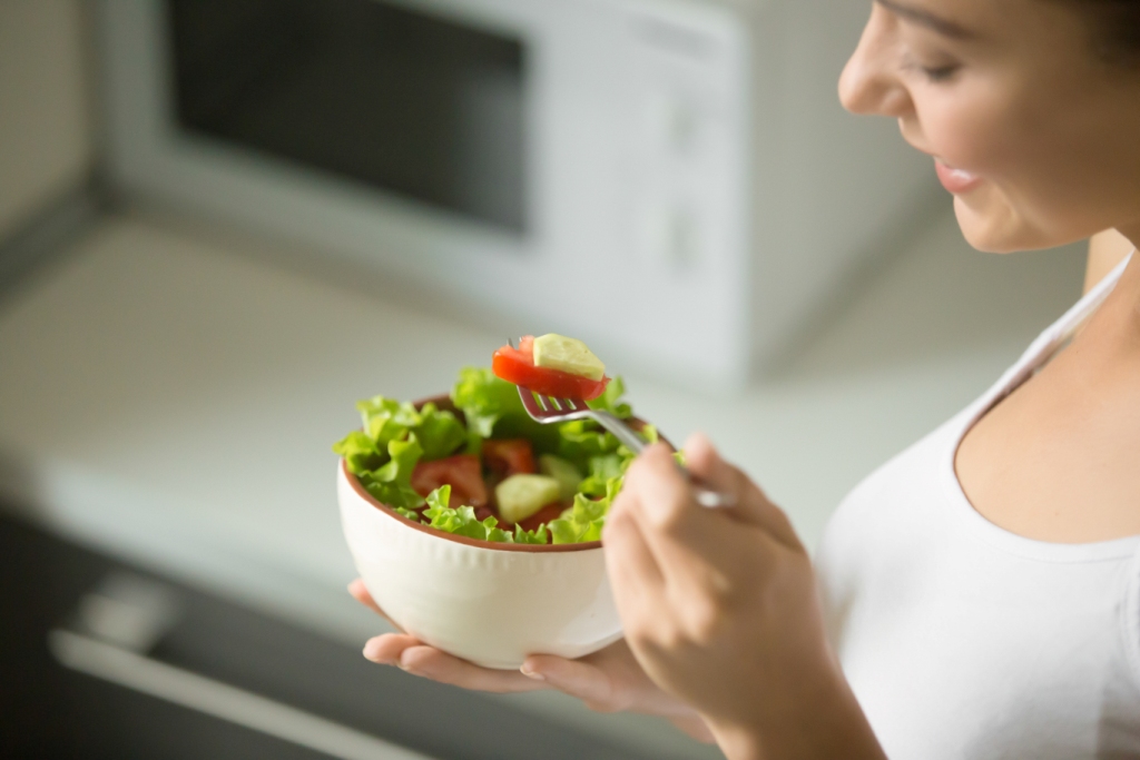 Mulher segurando saladeira branca com salada fresca numa cozinha moderna