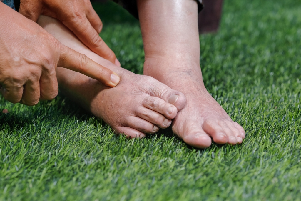 Pés descalços sobre relva verde com mão apontando para o dedão