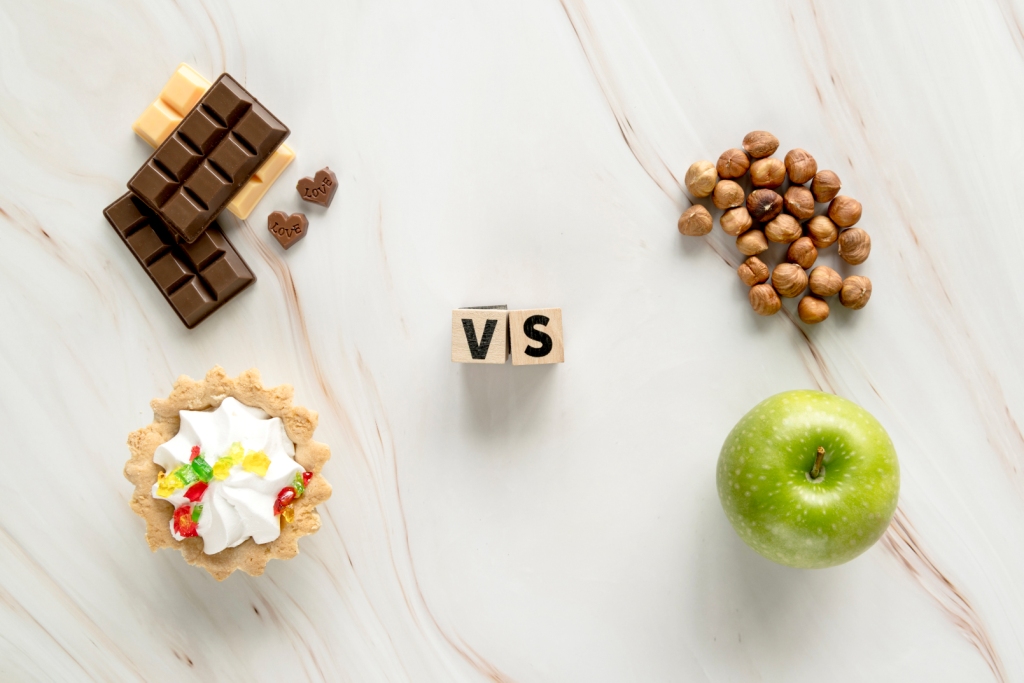 Comparação entre alimentos: chocolate e torta versus maçã verde e avelãs com cubos com as letras V e S no meio.