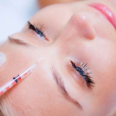 Pessoa a receber injeção na testa com mão enluvada