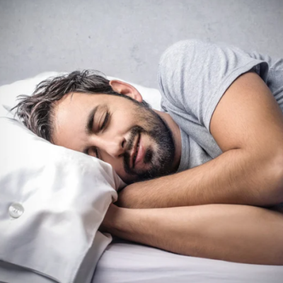 Homem a dormir de lado numa cama com almofada e lençóis brancos