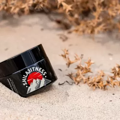 Frasco preto de creme SHILA FITNESS em areia com plantas secas ao fundo