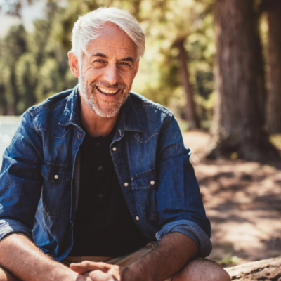 Homem sentado perto de lago com camisa azul de ganga e t-shirt preta