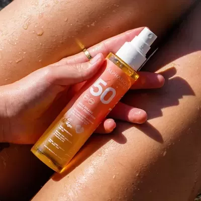 Frasco de óleo solar SPF 50 seguro por mão sobre pele molhada bronzeada