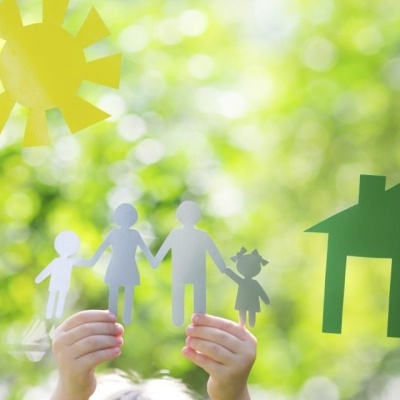 Recortes de papel de uma família, sol e casa segurados por mãos ao ar livre