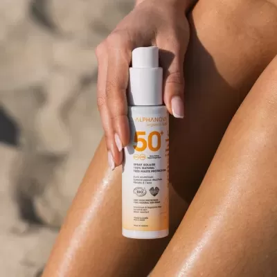 Spray solar ALPHANOVA FPS 50+ na mão, sobre pernas bronzeadas