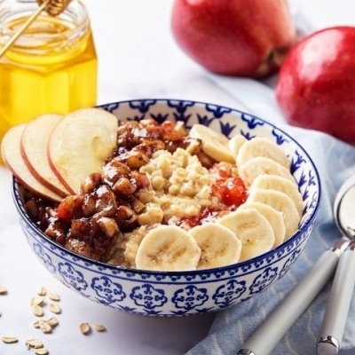 tigela de mingau de aveia com frutas e mel sobre mesa com maçãs e talheres