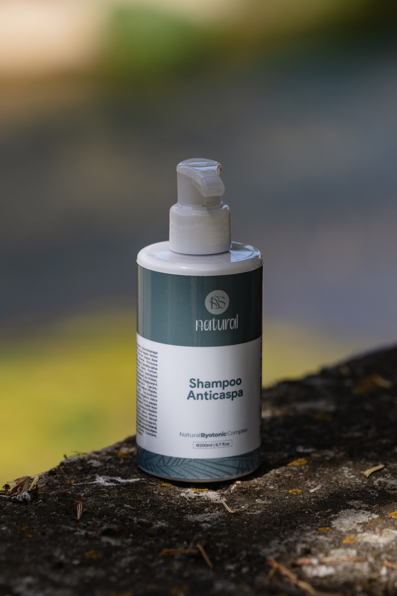 Shampoo Anticaspa Garrafas de shampoo anticaspa com tampa de bomba e rótulo azul esverdeado e branco sobre pedra.