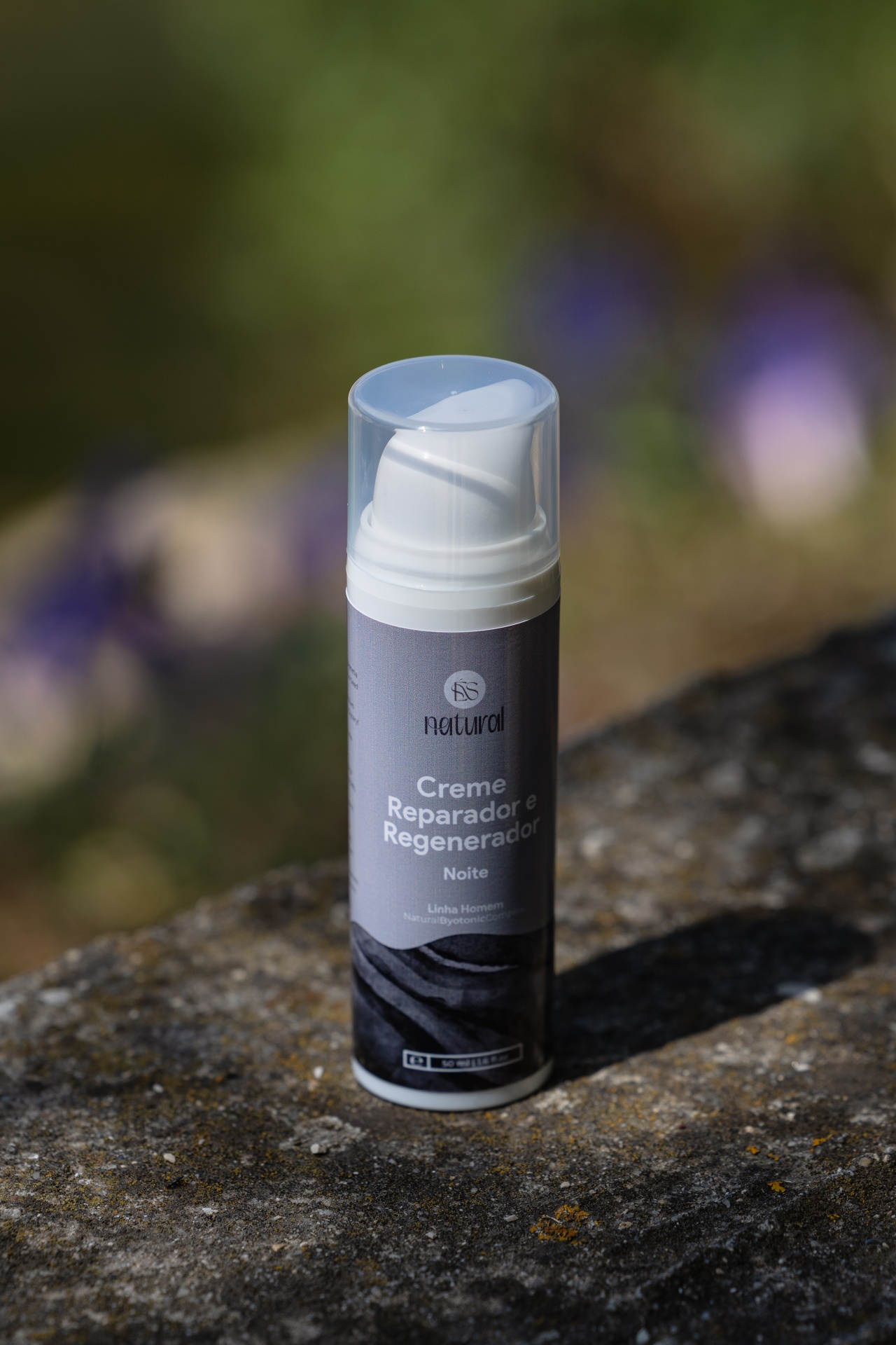 Creme Reparador e Regenerador Noite Frasco de creme reparador e regenerador para noite em ambiente natural sobre pedra.