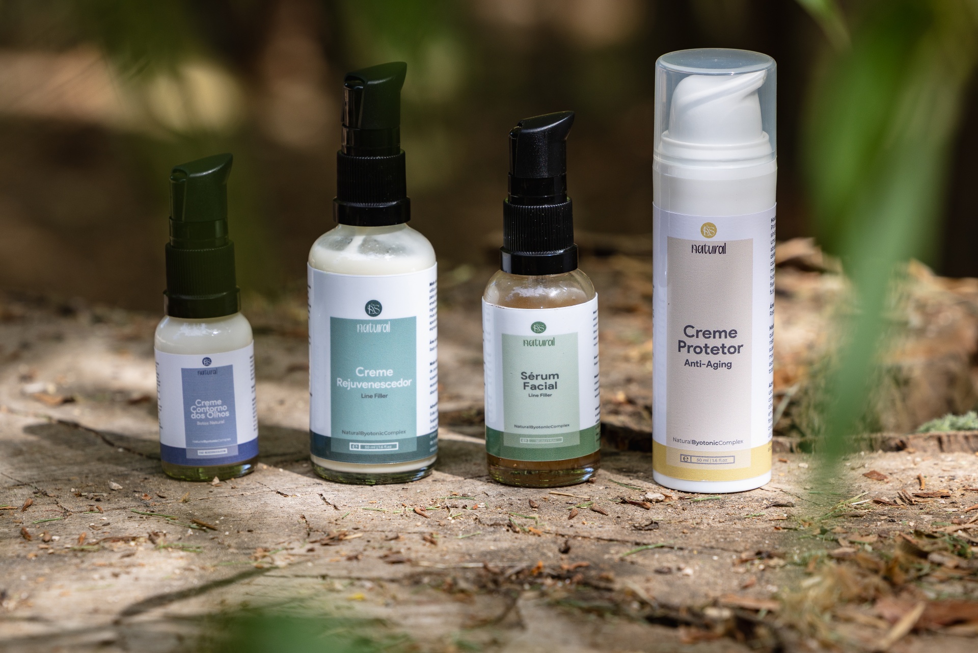Linha Anti-Aging (inclui 4 produtos) Frascos de produtos cosméticos naturais com rótulos coloridos e dispensadores pump sobre superfície de madeira.