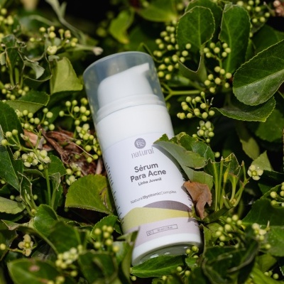 Frasco branco de sérum para acne sobre folhas verdes
