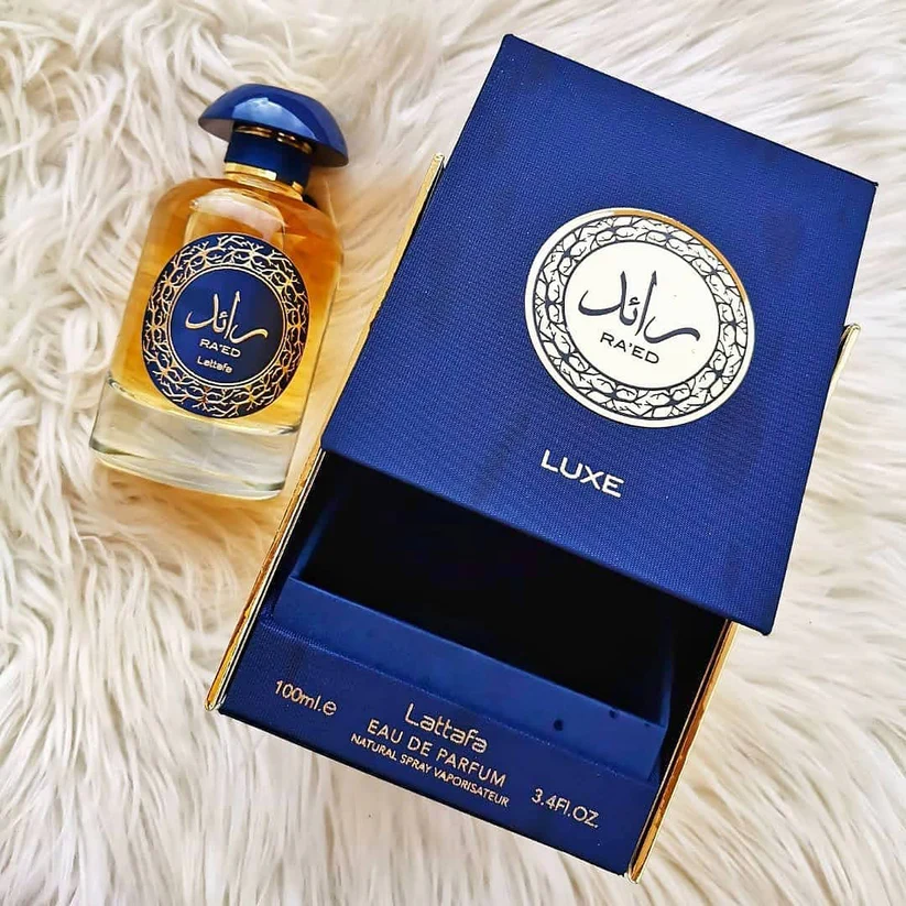 Frasco de perfume e caixa azul RA'ED LUXE Lattafa sobre fundo branco peludo