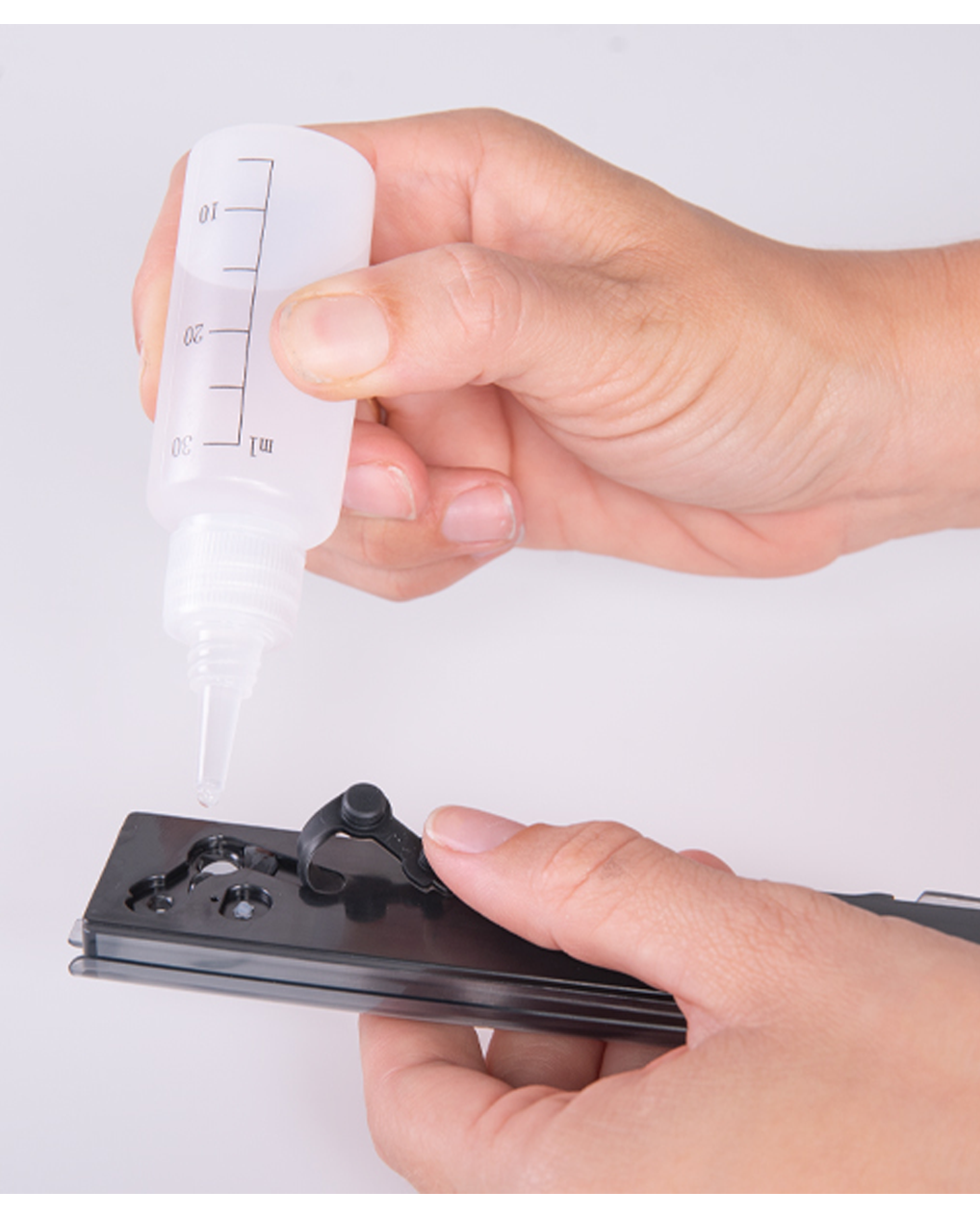 Frasco plástico translúcido com líquido sendo aplicado num dispositivo plástico preto