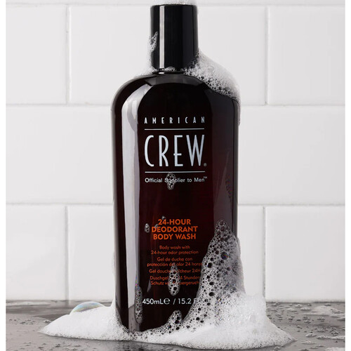 Frasco de sabonete líquido American Crew com espuma sobre superfície cinzenta e azulejos brancos