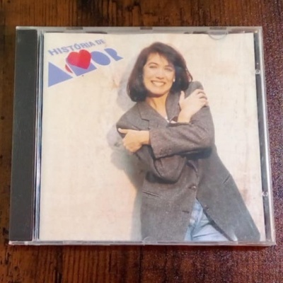 Capa de CD 'HISTÓRIA DE AMOR' com mulher sorridente vestindo casaco cinza