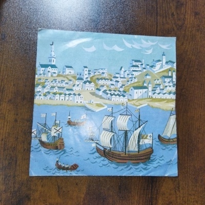 Ilustração de barcos antigos e cidade à beira-mar sobre mesa de madeira