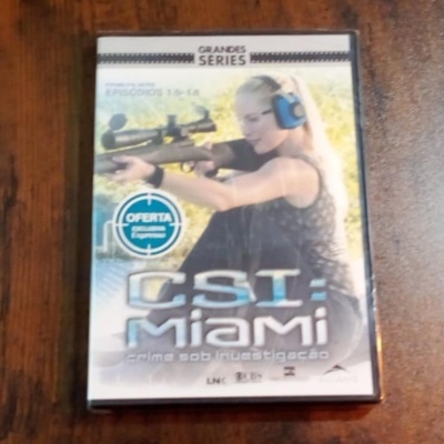 Capa de DVD da série CSI Miami com mulher loira a segurar um rifle e protetores auriculares azuis