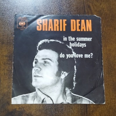 Capa de disco de vinil preto com texto SHARIF DEAN e imagem de homem com camisa aos quadrados