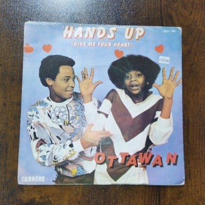Capa de single em vinil Hands Up de Ottawan com dois jovens e fundo azul