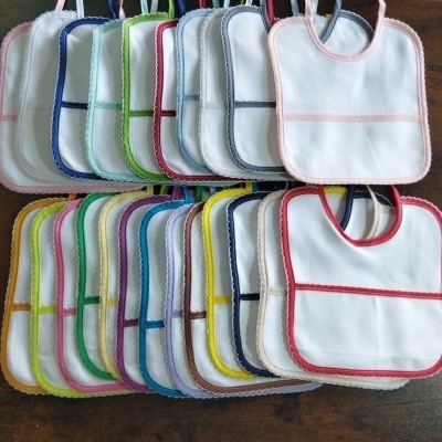 Babetes de tecido branco com bordas coloridas variados em superfície de madeira.