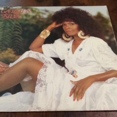 Capa de disco vinil com mulher em vestido branco e acessórios dourados sentada, texto CARMEN SILVA visível