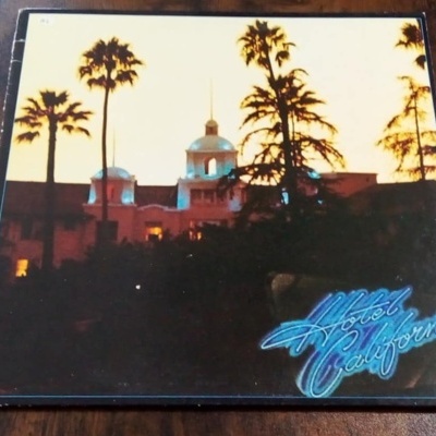 Capa de álbum de vinil Hotel California com imagem de hotel e palmeiras ao pôr do sol