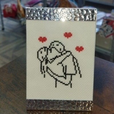 Quadro pequeno com bordado de casal a abraçar-se com corações vermelhos e moldura prateada