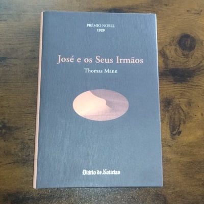 Capa de livro azul escuro com texto em rosa e branco sobre mesa de madeira.