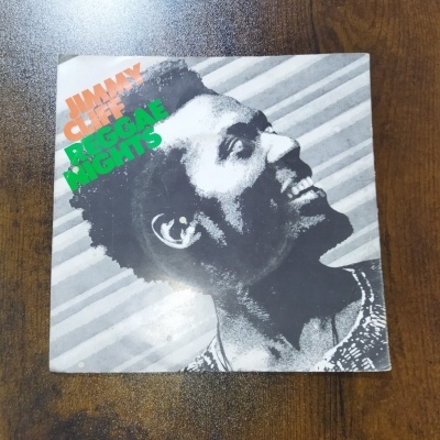Capa de álbum Jimmy Cliff Reggae Nights com imagem preto e branco e texto colorido sobre mesa de madeira