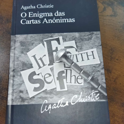 Livro O Enigma das Cartas Anónimas de Agatha Christie com capa preta e cinza e uma chave metálica em cima.