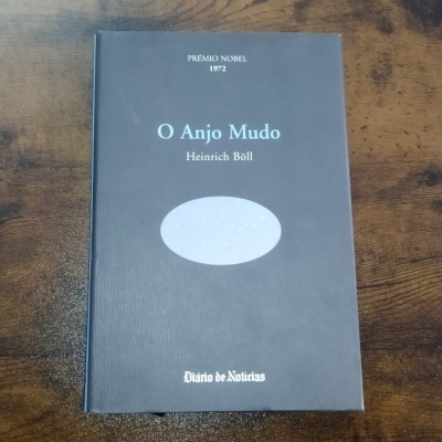 Capa de livro cinzenta com texto e oval branco, sobre mesa de madeira
